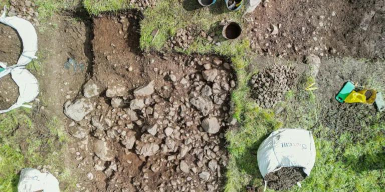 An area of ground excavated uncovering various sizes of rocks. Bags of soil surround the excavation site.