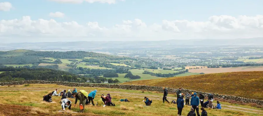 A large group of people in a field with a view of hills in the background.