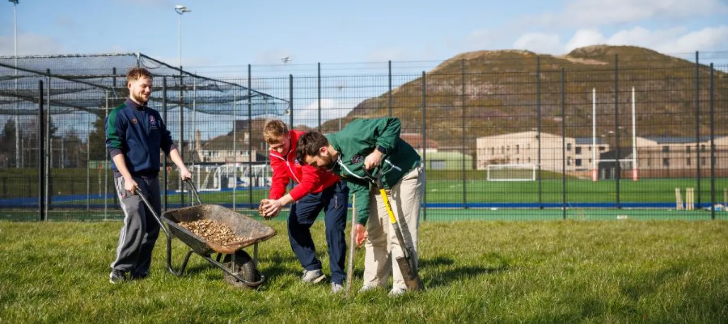 three people gathered round a wheelbarrow on a grassy lawn