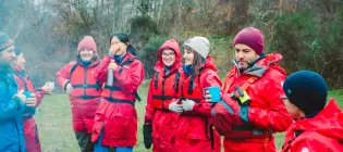 Students and staff wearing red life jackets and coats stand outside laughing and smiling