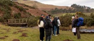 A group of interdisciplinary students listen to the community ranger at the Pentlands forest restoration site to learn about tree planting as part of the Students and Change agents course at EFI.