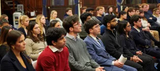 An audience of people sit watching a speaker