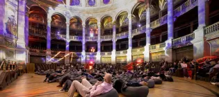 people sit on beanbags in a large hall, with light projections case onto the walls and ceiling