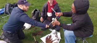 three people examine soil using tools