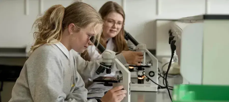 A young person looking into a microscope, with a school pupil also examining a microscope in the background
