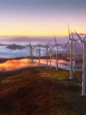 Wind turbines on a mountain at sunset, with clouds below the mountain peak