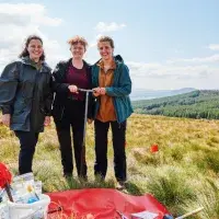 Three people standing in a field with a soil corer.
