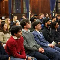 An audience of people sit watching a speaker