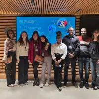 A group of people stand in front of a screen, smiling