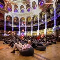 people sit on beanbags in a large hall, with light projections case onto the walls and ceiling
