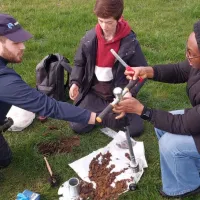 three people examine soil using tools