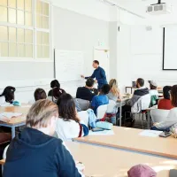 A group of people in a classroom watch a person at a whiteboard