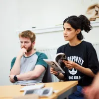 Two people sit at a desk, with one holding a book
