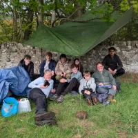A group of people sheltering under a tarp outdoors and smiling for a photo.