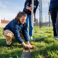 A student athlete plants a sapling at Peffermill Playing Fields, helped by other students