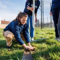 A student athlete plants a sapling at Peffermill Playing Fields, helped by other students