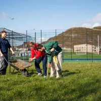 three people gathered round a wheelbarrow on a grassy lawn