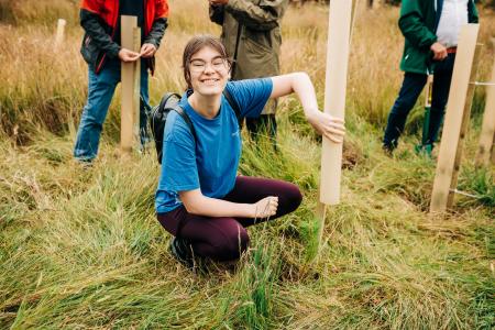EUSA President crouching down and smiling while planting a tree at Drumbrae.