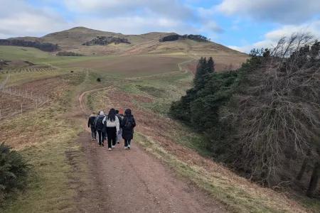 Students in the distance walking along a path with hills on either side.