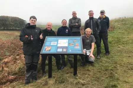 Forest and Peatland Community Ranger Julie with volunteers from the Friends of the Pentlands standing by the new interpretation panel at Rullion Green.