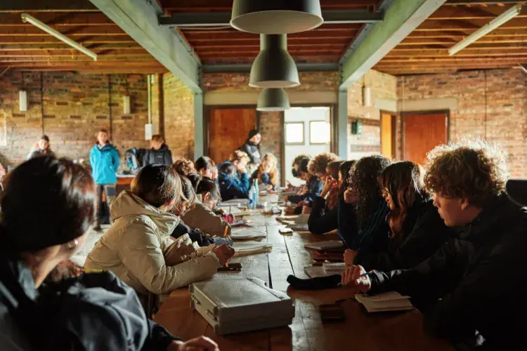 People sitting at a long table with notebooks listening to a speaker.