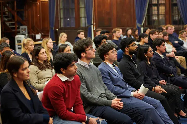 An audience of people sit watching a speaker