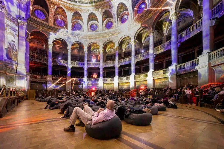 people sit on beanbags in a large hall, with light projections case onto the walls and ceiling