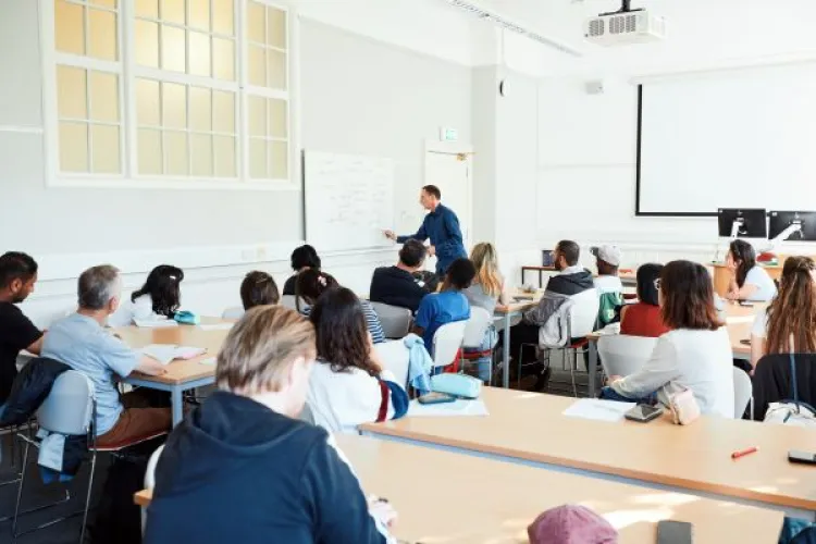 A group of people in a classroom watch a person at a whiteboard