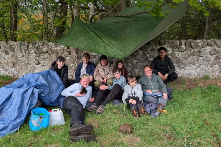 A group of people sheltering under a tarp outdoors and smiling for a photo.