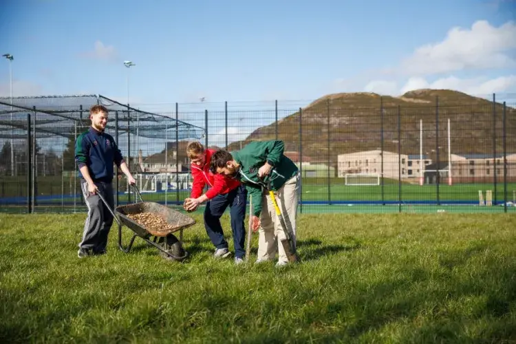 Student athletes with a wheelbarrow at Peffermill Playing Fields with Arthurs Seat in the background