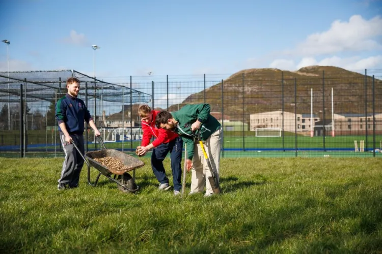 three people gathered round a wheelbarrow on a grassy lawn