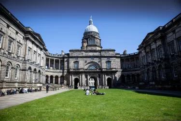 A photo of a lawn with people sitting on it, with an old domed building in the background