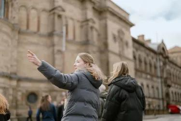 Two people outside a large building, one of them pointing