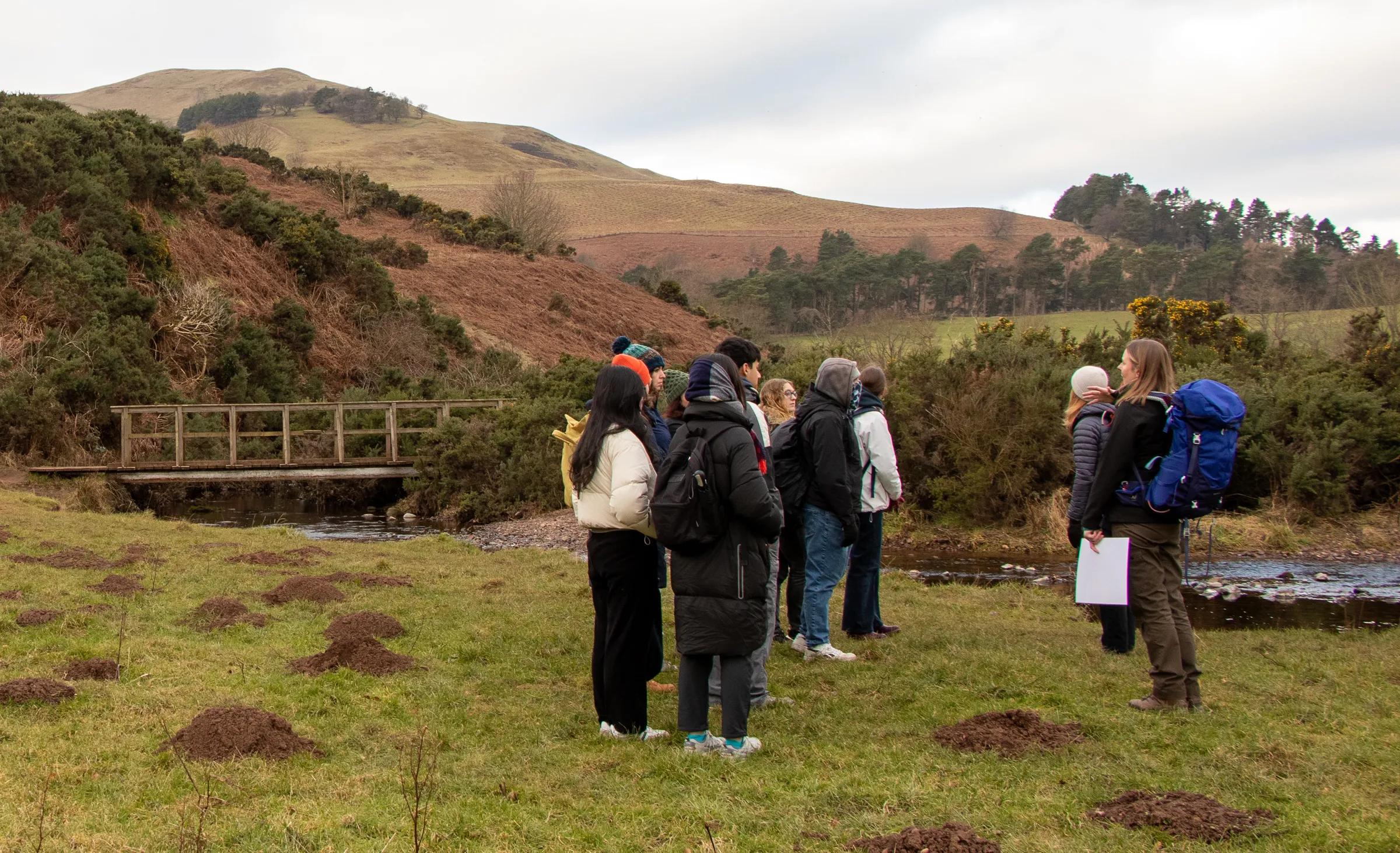A group of interdisciplinary students listen to the community ranger at the Pentlands forest restoration site to learn about tree planting as part of the Students and Change agents course at EFI.