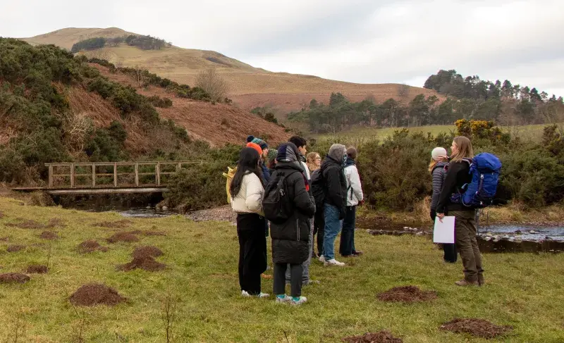 A group of interdisciplinary students listen to the community ranger at the Pentlands forest restoration site to learn about tree planting as part of the Students and Change agents course at EFI.