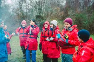 Students and staff wearing red life jackets and coats stand outside laughing and smiling