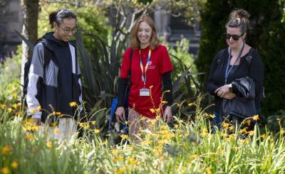 University staff and students smile at bright yellow flowers growing on campus