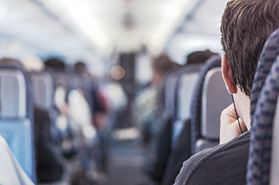 looking down the aisle of a plane or train, over shoulder of person wearing headphones.